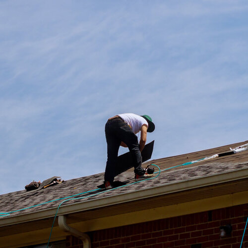 Worker standing on a roof and installing shingles.